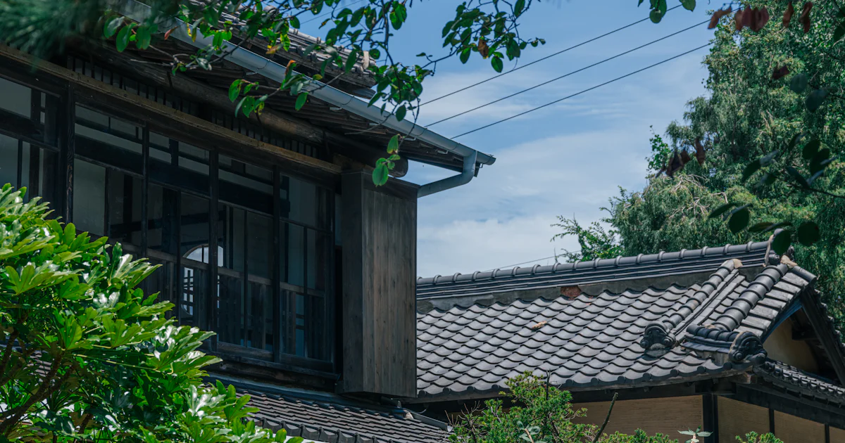 木々に囲まれた古い日本家屋の屋根と外壁