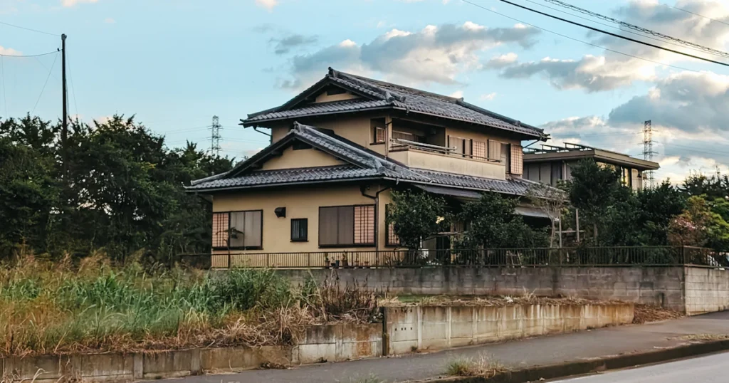 草が伸びた敷地に建つ、雨戸を閉めた日本の二階建て住宅